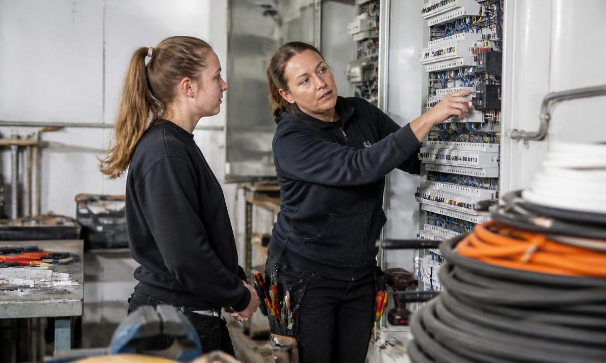 Elektrotechnikerin erklärt einer Auszubildenden einen Schaltschrank